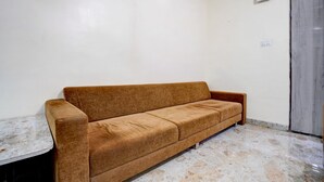 A room with a brown sofa, a white wall, a door, and a tiled floor. - Super Collection O Daulatabad Fort (Chhatrapati Sambhajinagar)