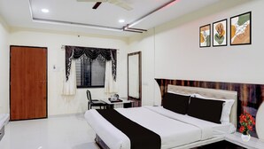 A bedroom with a bed, a desk, a chair, a ceiling fan, and artwork on the wall. - Super Collection O Daulatabad Fort (Chhatrapati Sambhajinagar)