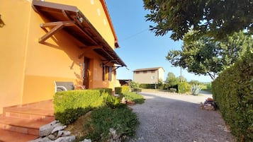 Un edificio con facciata gialla, vialetto sterrato e siepi curate.