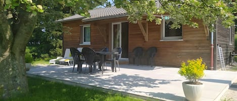 A wooden cabin with a patio table and chairs, surrounded by greenery.