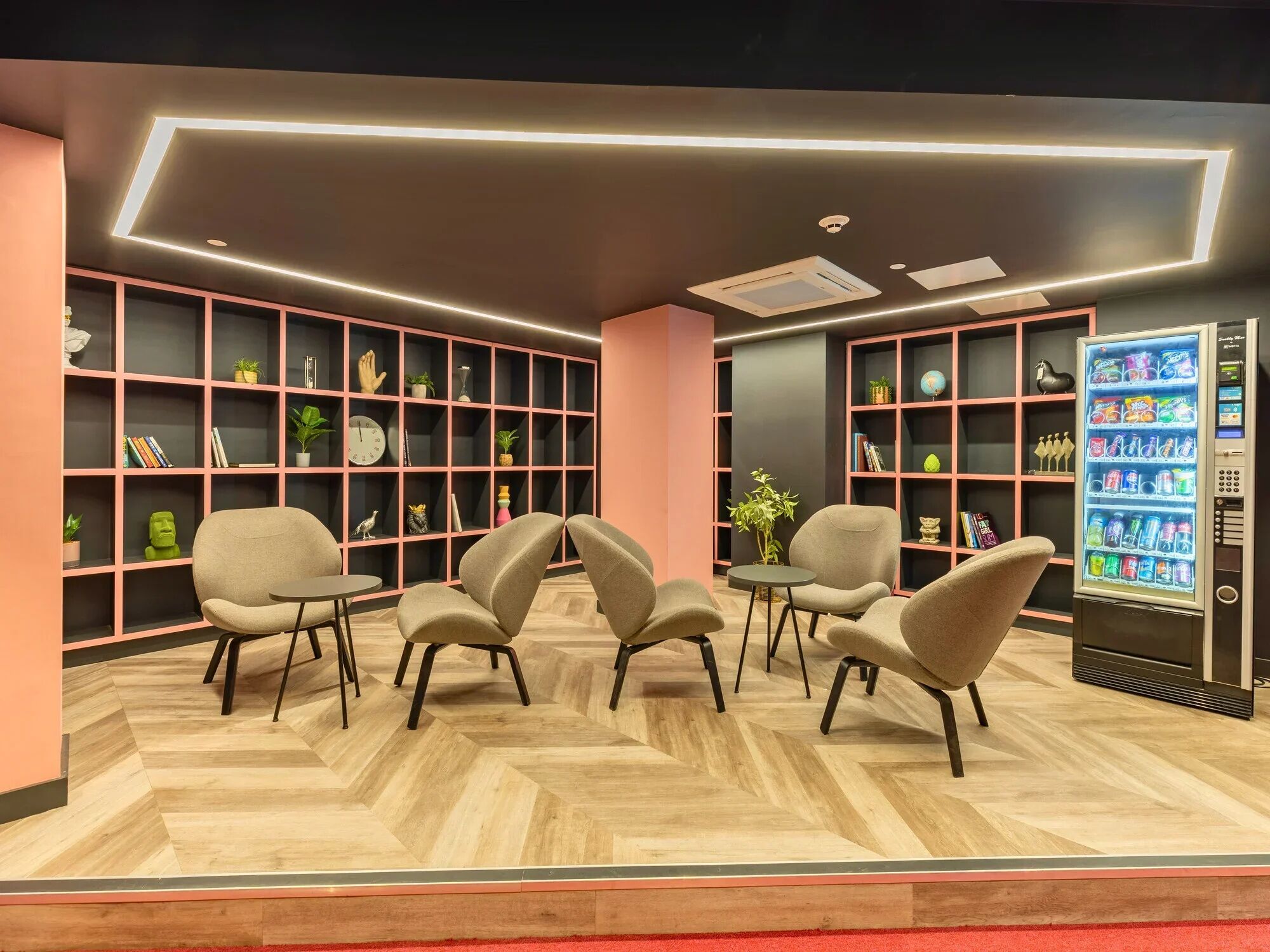 A modern lounge area with seating, bookshelves, and a vending machine.