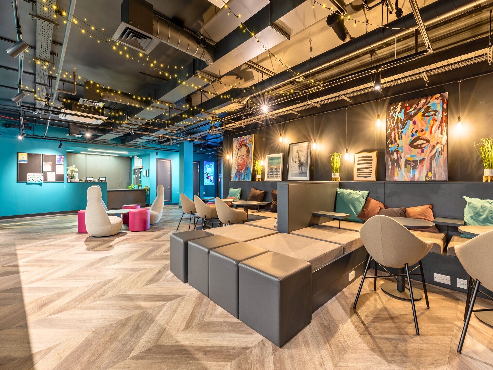A modern office space with a herringbone wood floor, modular seating, and a variety of wall art.