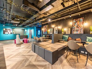 A modern office space with a herringbone wood floor, modular seating, and a variety of wall art. - Student Only Crown House (Brighton and Hove)