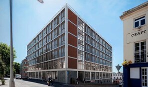 Ein mehrgeschossiges Gebäude mit modernem architektonischen Design, das Glas- und Backsteinfassade kombiniert und einen Eingang mit auffälligem Vordach im Erdgeschoss hat.