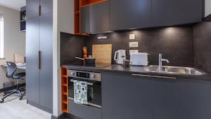 A modern kitchen with dark cabinetry, a built-in oven, a coffee maker, and a toaster. - Student Only Crown House (Brighton and Hove)