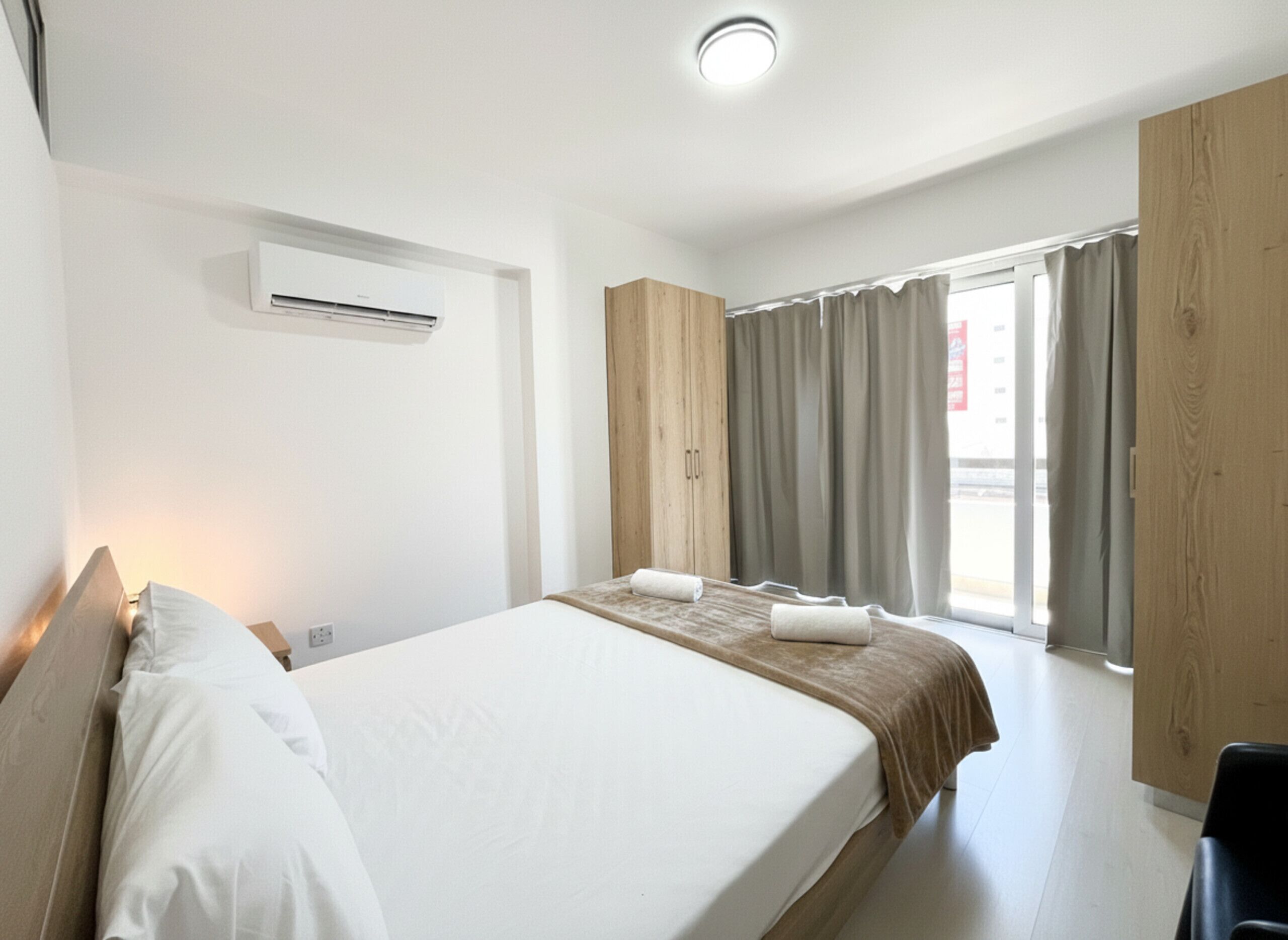 Een hotelkamer met een bed, een raam met gordijnen, een houten kledingkast en een airconditioning.