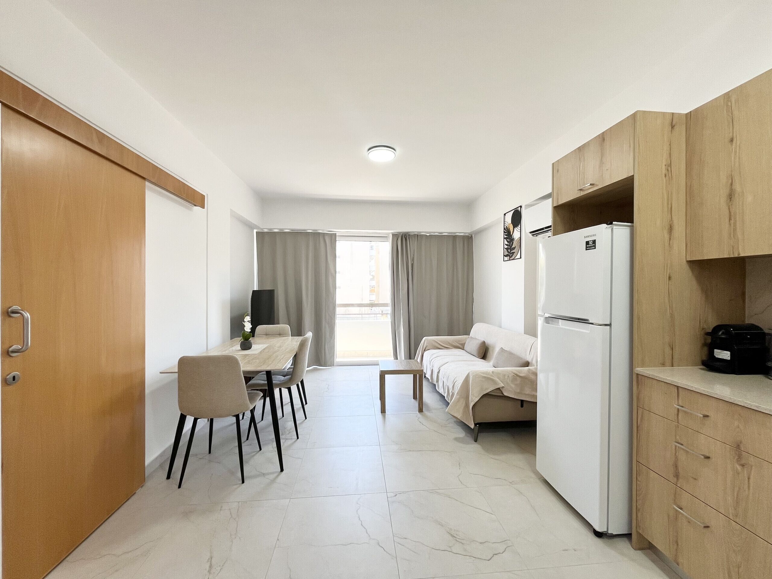 Cozinha compacta com geladeira, armários de madeira e área de refeições com mesa e cadeiras.