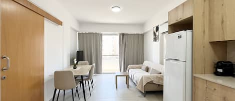 Una cocina compacta con refrigerador, armarios de madera y un comedor con mesa y sillas.