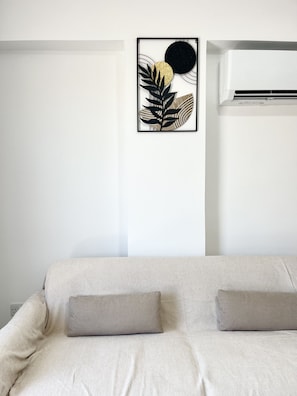 A bedroom with a bed, two pillows, a wall-mounted air conditioner, and a framed artwork. - STAY Finikoudes Nest 3 (Larnaca)