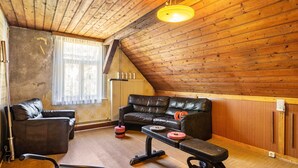 A loft-style room with a wooden ceiling, a leather sofa, a workout bench, and various weights.