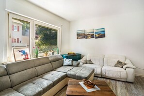 A living room with a sectional sofa, a smaller sofa, a coffee table, and a chess set. There are three framed pictures on the wall.