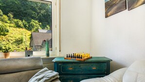A room with a view of a green landscape, a chessboard on a dresser, and two sofas.