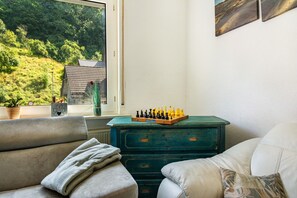 A room with a view of a green landscape, a chessboard on a dresser, and two sofas.