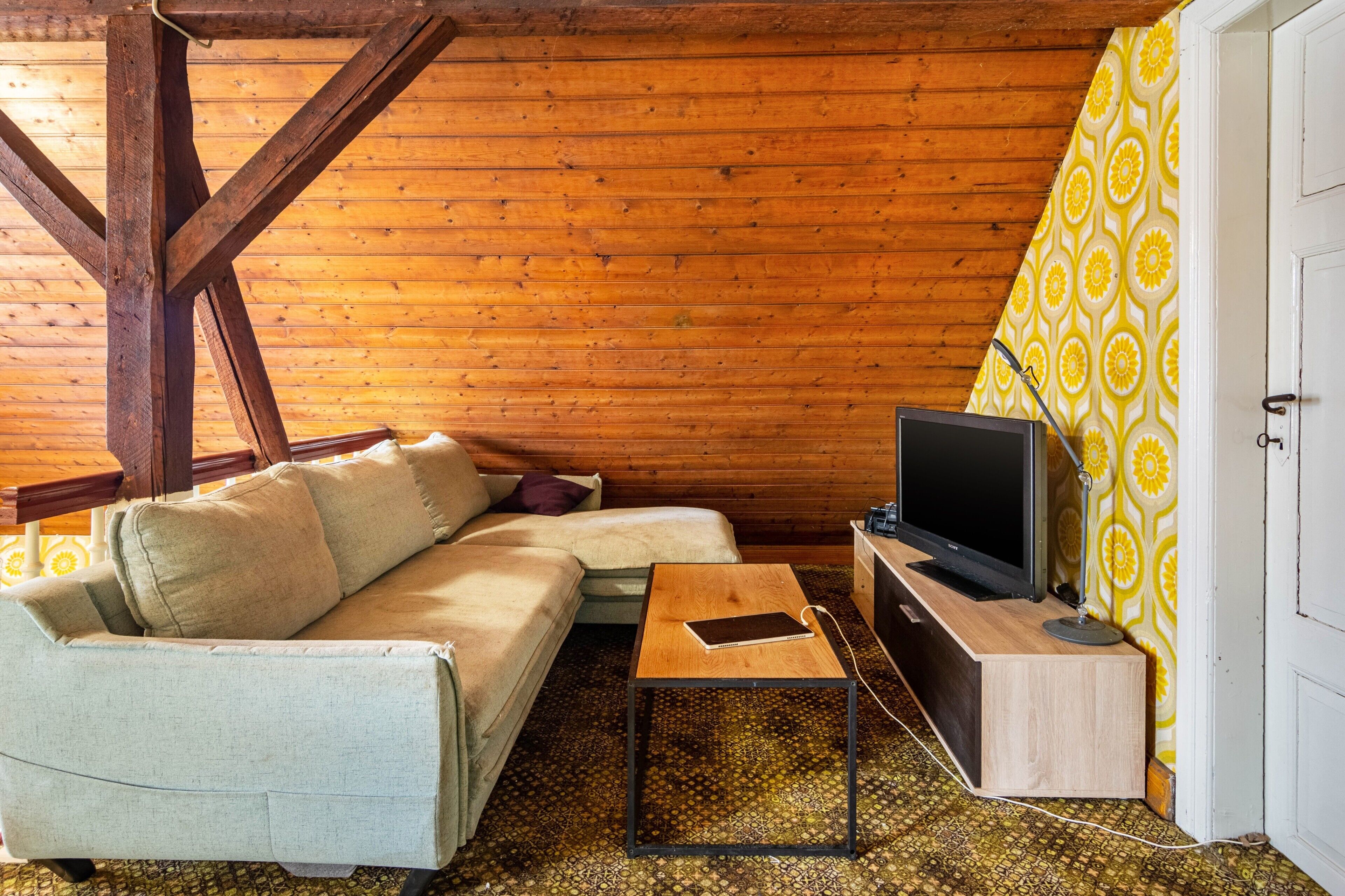 Une pièce chaleureuse avec un plafond en bois, un canapé, une petite table, un téléviseur et un rideau à motifs.