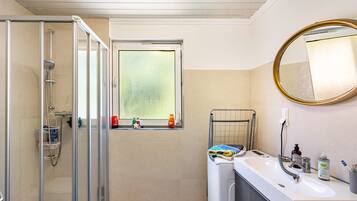 Ein Badezimmer mit Duschkabine aus Glas, einem Fenster mit Blick, einem Waschbecken mit Spiegel und Pflegeprodukten.
