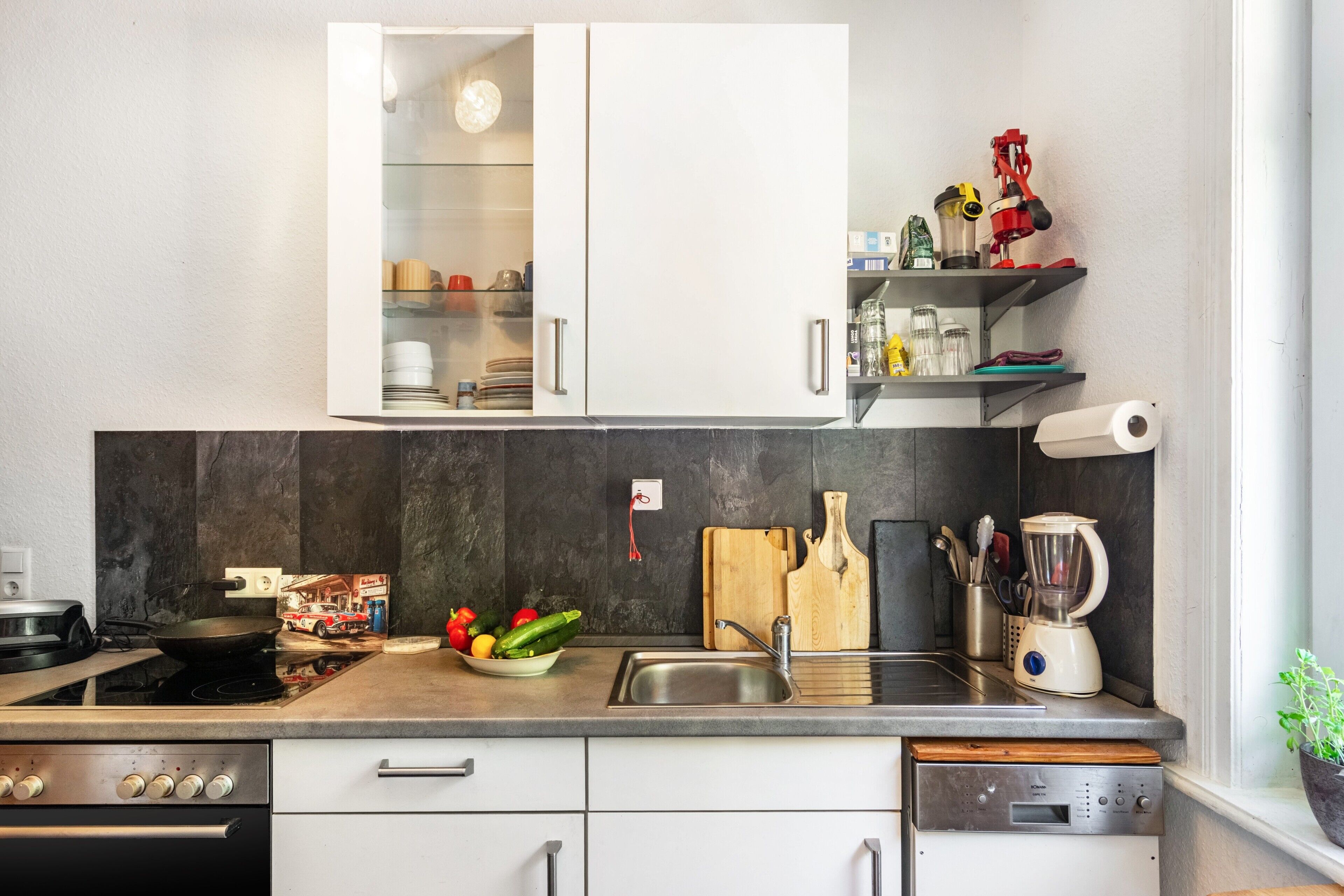 Une cuisine moderne avec des meubles blancs, un four encastré, un évier et un lave-vaisselle.