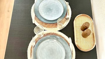 Une table à manger avec deux assiettes, une fourchette, un couteau et une petite bouteille, le tout disposé sur une table sombre recouverte de sets de table en fibres tressées.