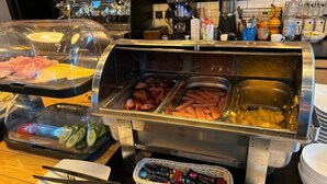 Un buffet proposant divers plats, notamment des tranches de concombre, des saucisses et un récipient contenant des tranches de fromage.