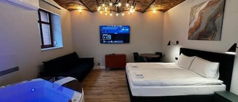 A room with a bed, a massage table, a TV, and a painting on the wall.