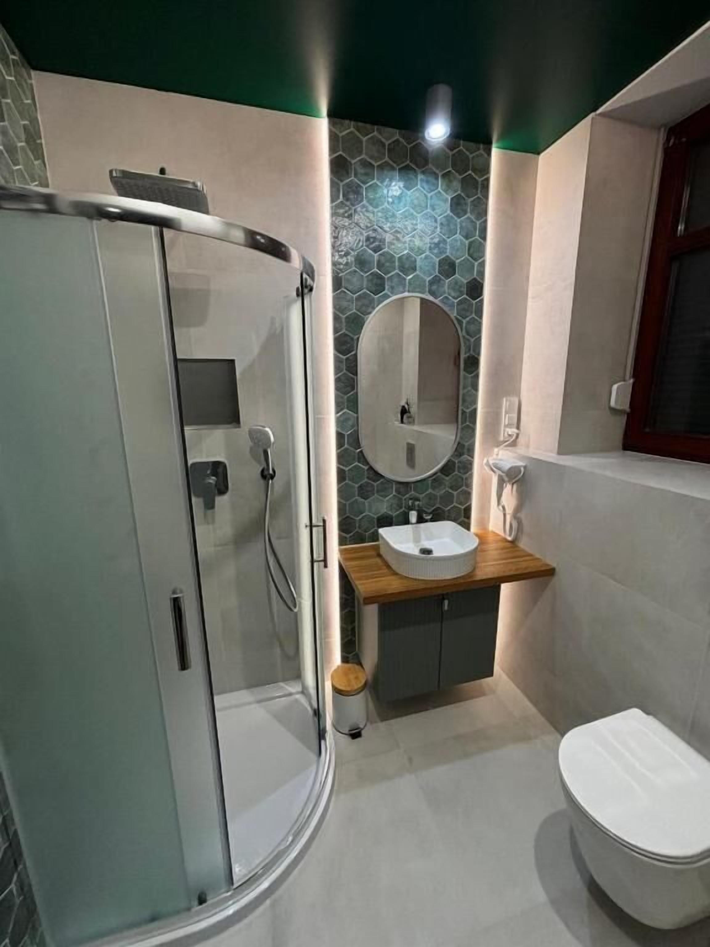 Ein Badezimmer mit Duschkabine aus Glas, einem Holzwaschtisch mit Waschbecken, einem Spiegel und einer Toilette.
