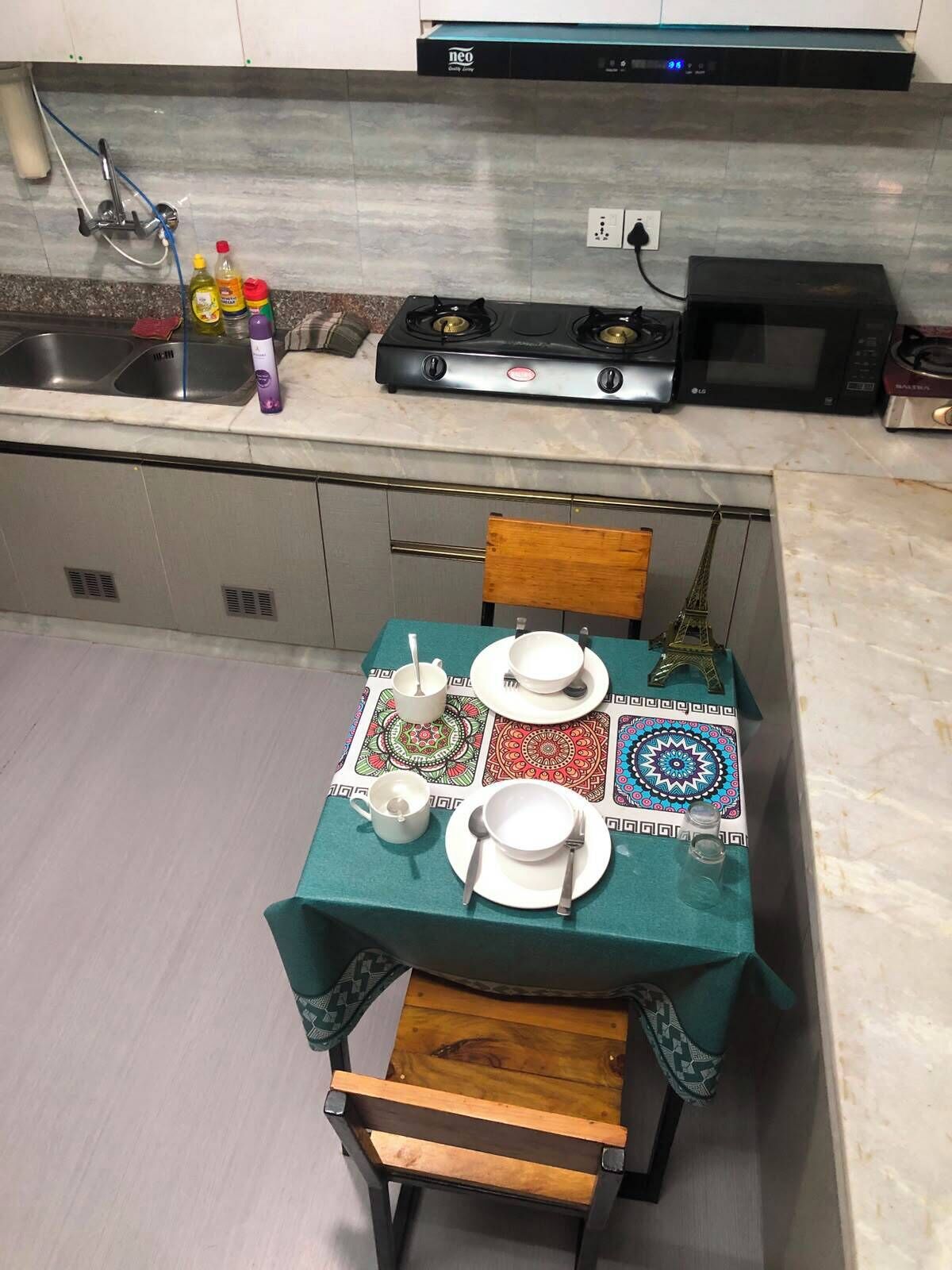 Una cocina con estufa a gas, microondas y lavamanos. Hay una mesa dispuesta con platos, tazas y una Torre Eiffel decorativa.