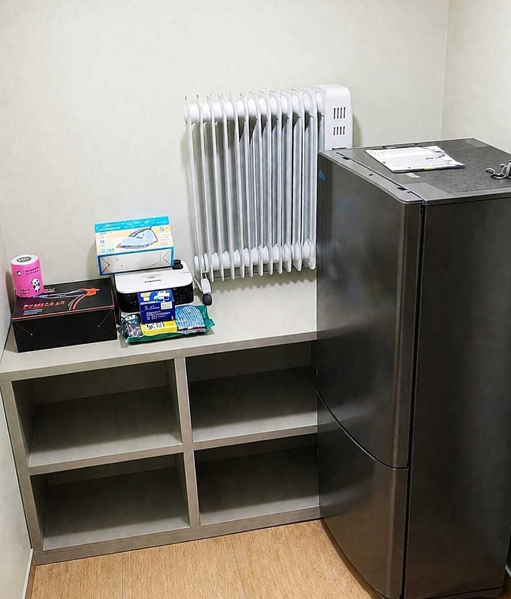 Een kleine keuken met een inbouwkoelkast, een witte radiator en een klein plankje met diverse spullen.