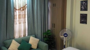Um quarto com cama, um sofá verde com almofadas, um ventilador de teto e um lustre.