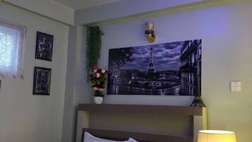 A hotel room with a bed, a nightstand with a lamp, a wall clock, and a framed picture of the Eiffel Tower.