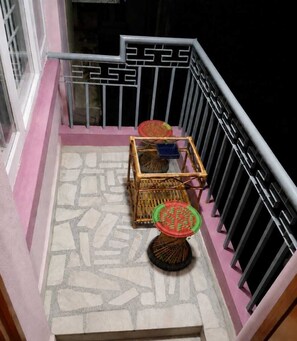 A balcony with a metal railing, a small table, and two wicker chairs. - PARIS APARTMENT (Kathmandu)