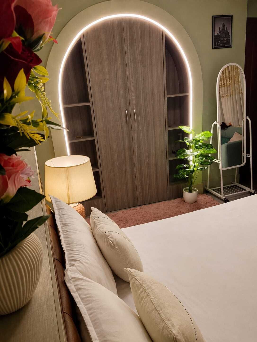 Un dormitorio con cama, lámparas de noche, armario, espejo y planta en maceta.