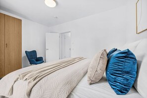 A bedroom with a bed, a chair, and a wardrobe. - Brand-New Luxury Apartment with Baltic Sea Views in Travemünde (Lübeck)