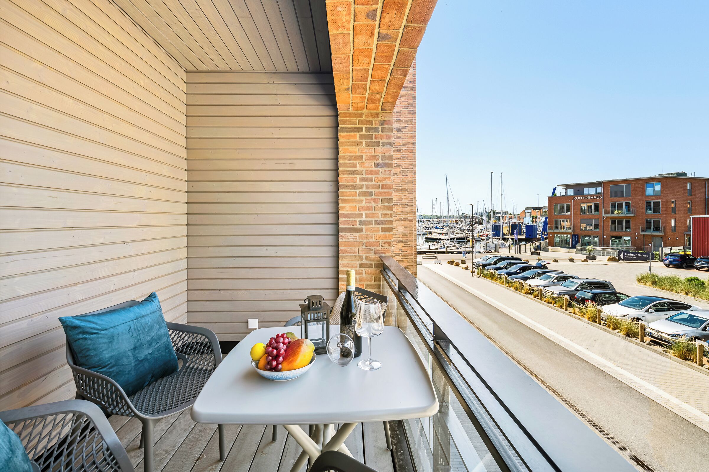 A balcony with a table set for two, a bowl of fruit, and a bottle of wine.