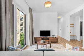 A modern living room with a flat-screen TV, wooden furniture, and a large window. - Brand-New Luxury Apartment with Baltic Sea Views in Travemünde (Lübeck)