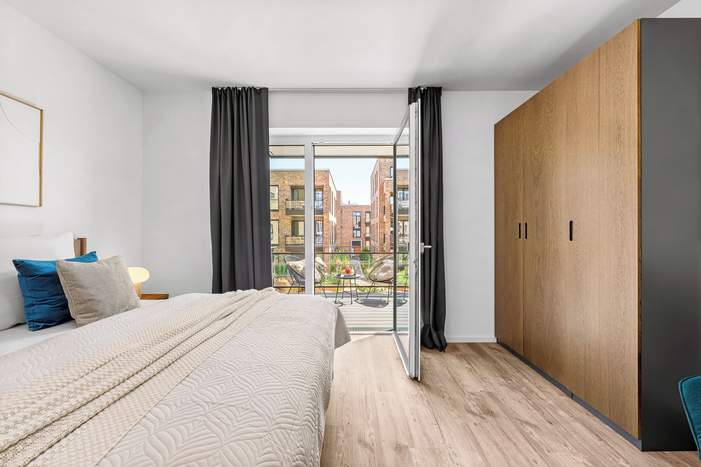 A modern bedroom with a large bed, a wardrobe, and a balcony with a city view.