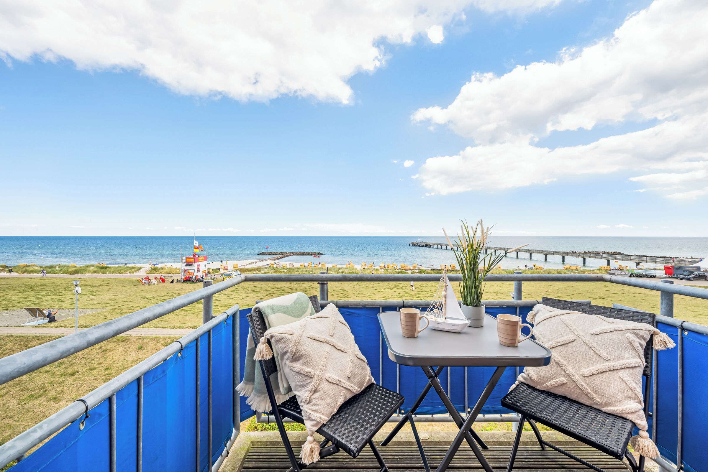 A deck with two chairs, a table, and a view of the beach and sea.