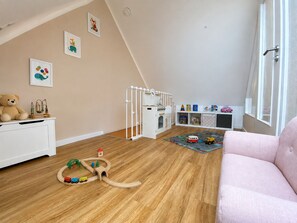 Una sala de juegos infantil con un andamio de madera, un armario blanco y un sofá rosa.