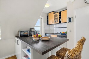 Una cocina compacta con encimera oscura, un tostador, un hervidor y un cuenco con fruta.