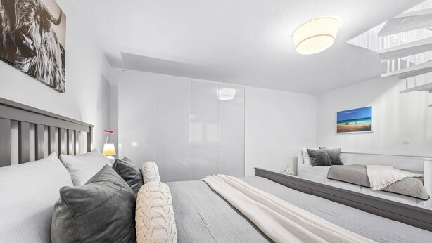 Um quarto moderno com uma cama grande, uma mesinha de cabeceira, um espelho e um quadro na parede.