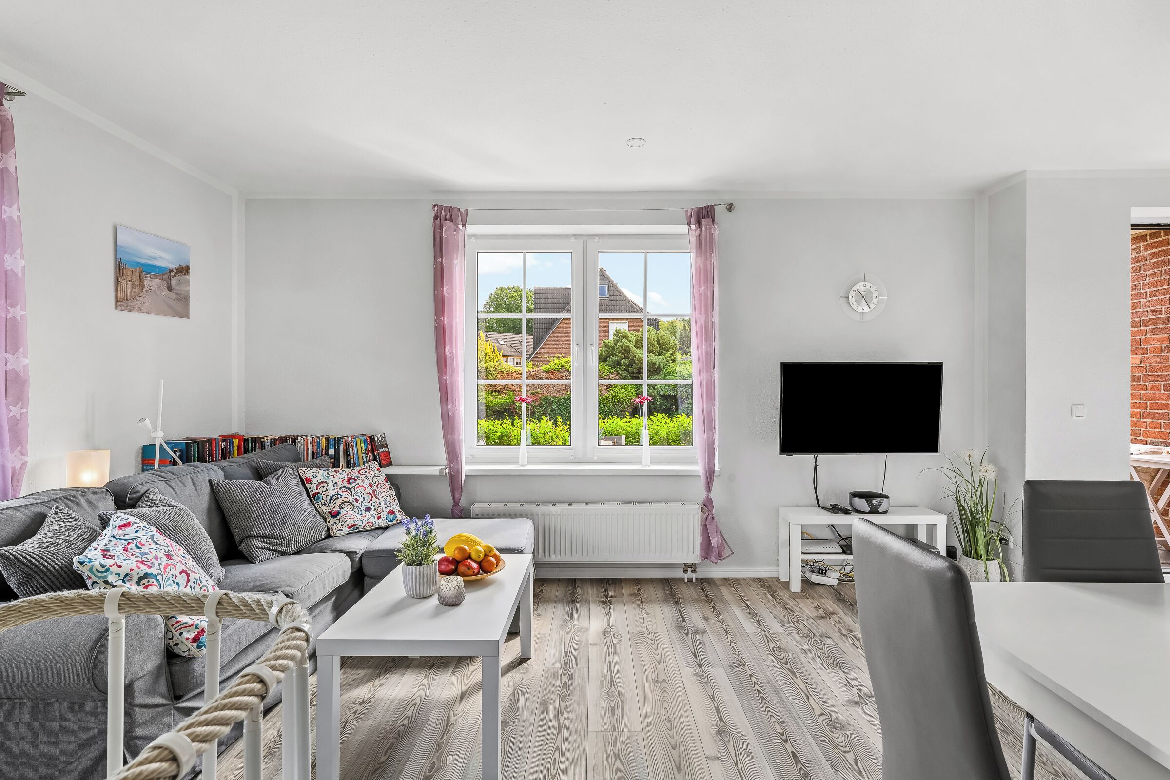 A modern living room with a sofa, a coffee table with fruit, a TV, and a window with curtains.