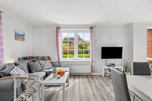 A modern living room with a sofa, a coffee table with fruit, a TV, and a window with curtains.