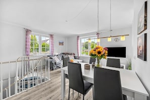 Una sala de estar moderna con comedor, una escalera y ventanas grandes.