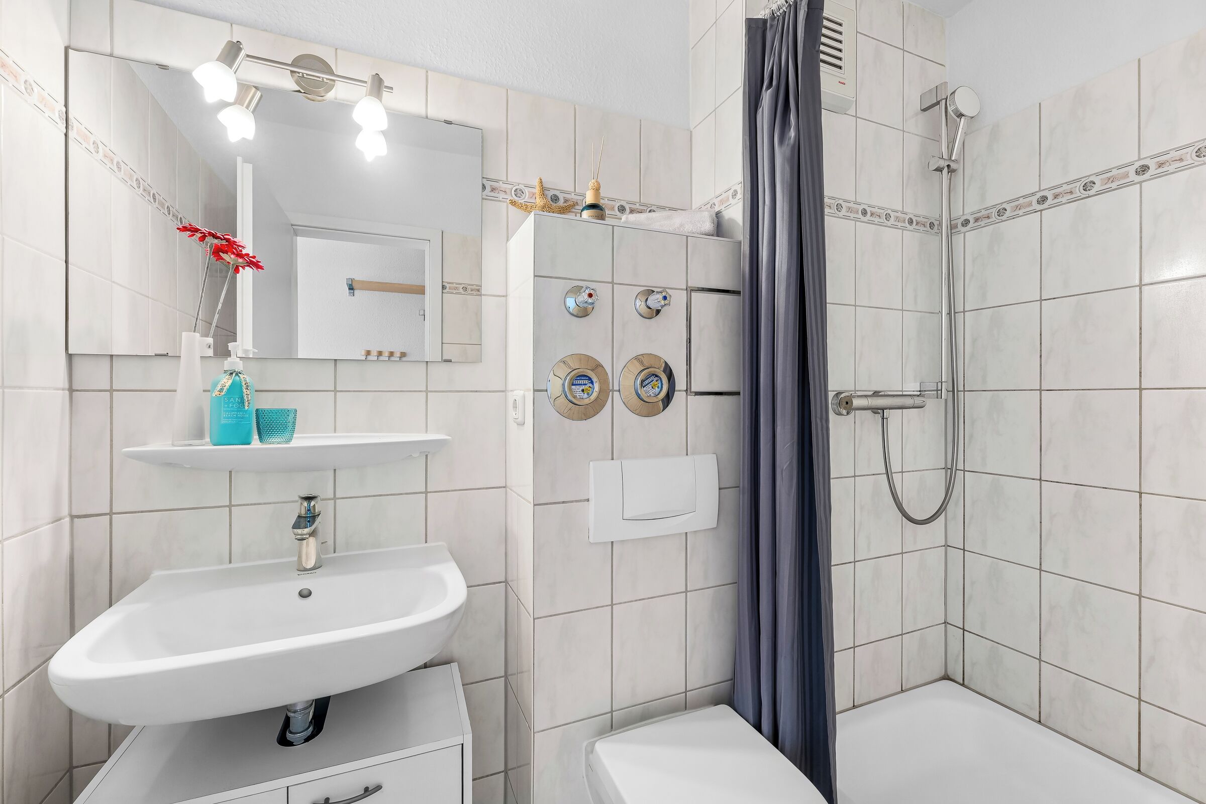 Un bagno moderno con lavandino, specchio e doccia bianchi.