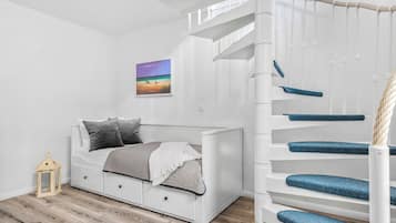 A white room with a bed, a small table, and a staircase.