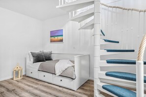 A white room with a bed, a small table, and a staircase.