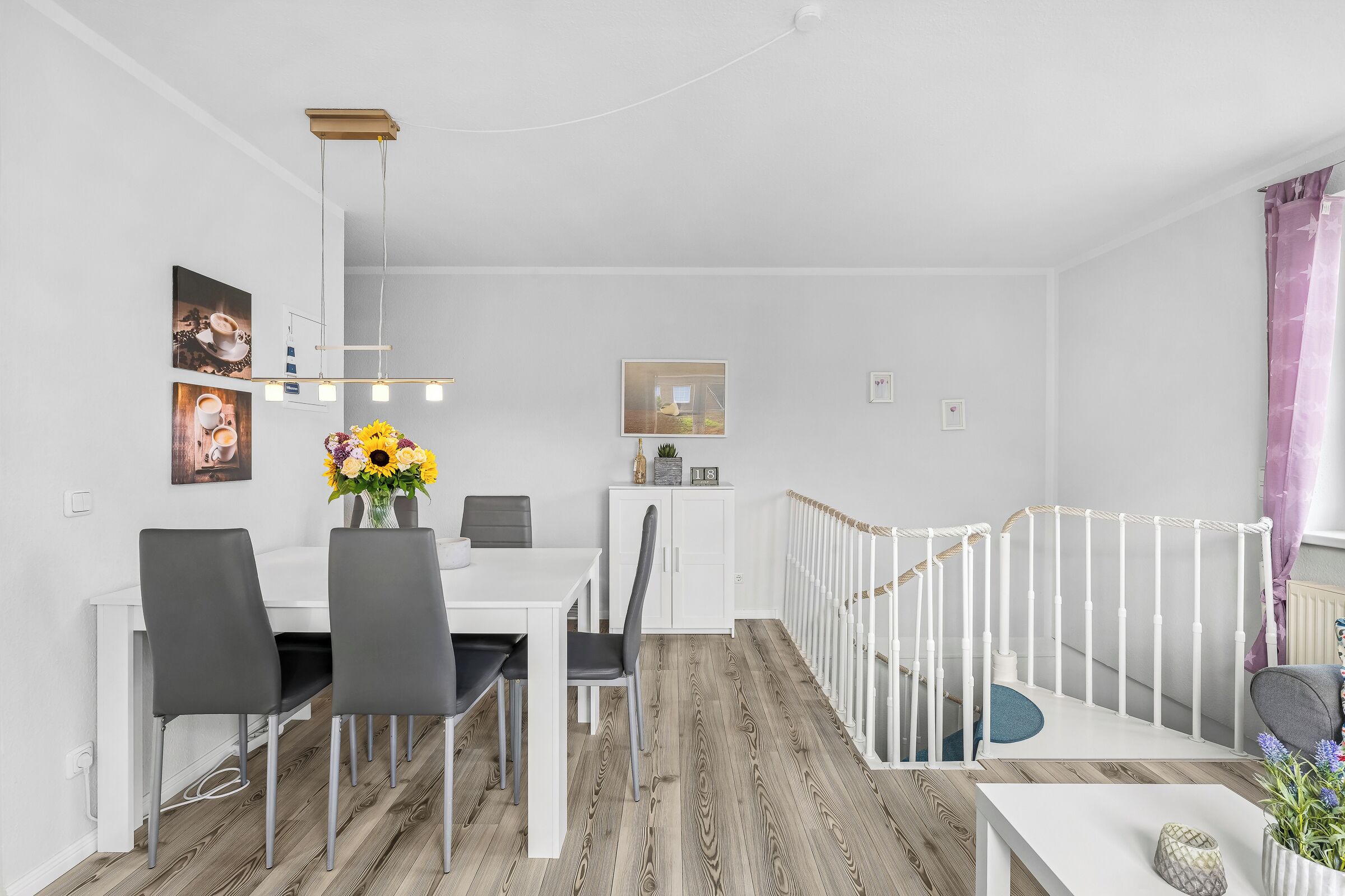 Un comedor moderno con una mesa blanca, sillas negras y un jarrón de girasoles.