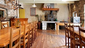 A rustic dining area with wooden tables and chairs, a stone wall, a fireplace, and a television.