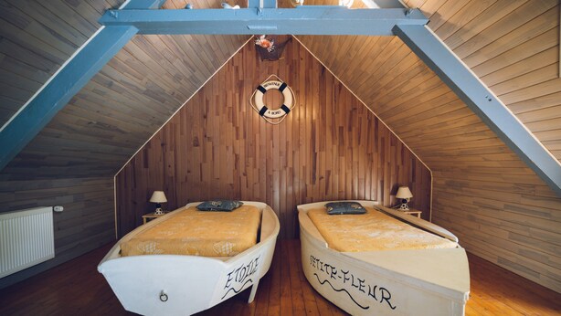 A room with a sloped ceiling, two beds with decorative headboards, a life preserver hanging from the ceiling, and a wooden floor.