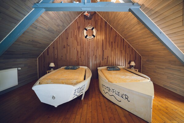 A room with a sloped ceiling, two beds with decorative headboards, a life preserver hanging from the ceiling, and a wooden floor.