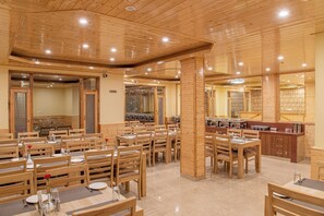 En restaurang med trämöbler och en central pelare. Borden är dukade med tallrikar och glas.