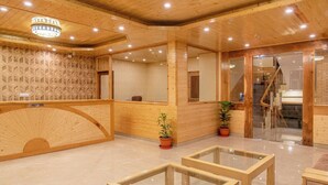 Zona de recepción con un mostrador de madera, cartel de recepción, una escalera y plantas en macetas.